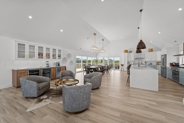 living room with light wood finished floors, beverage cooler, high vaulted ceiling, and indoor bar