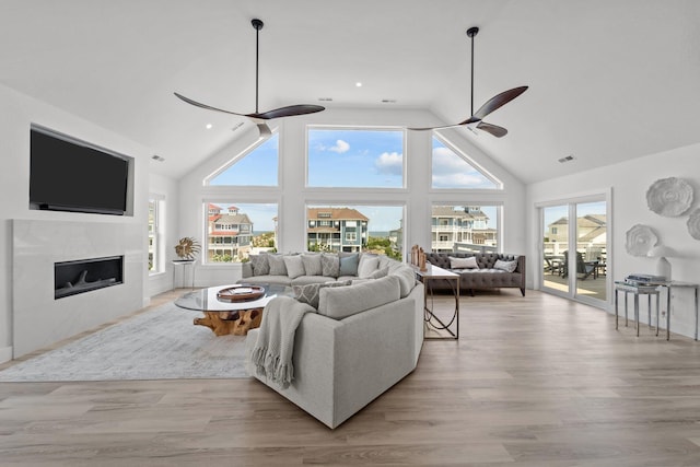 living room featuring a ceiling fan, light wood-style floors, a fireplace, and high vaulted ceiling