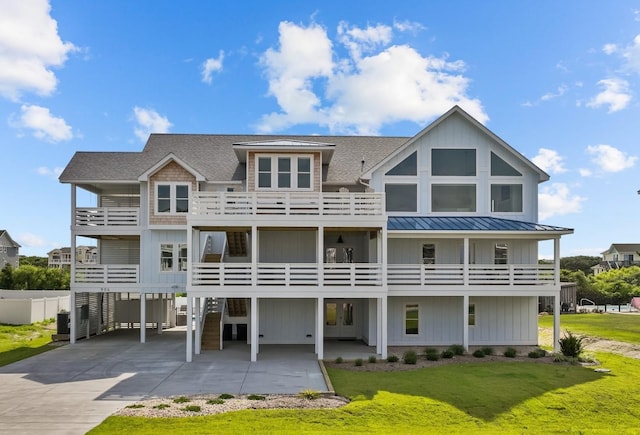 rear view of property featuring metal roof, concrete driveway, a lawn, a carport, and a standing seam roof