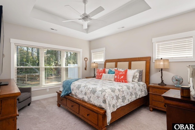 bedroom featuring light carpet, visible vents, baseboards, ceiling fan, and a tray ceiling