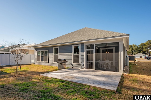 rear view of property featuring a yard, a sunroom, roof with shingles, and fence