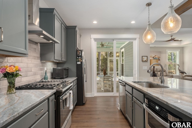 kitchen with wall chimney exhaust hood, a sink, stainless steel appliances, gray cabinetry, and backsplash