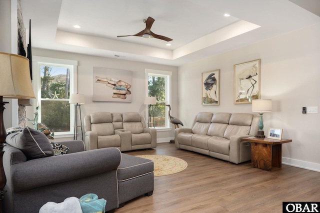 living room featuring a ceiling fan, a raised ceiling, baseboards, and wood finished floors