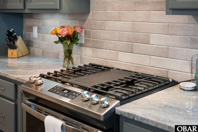 kitchen featuring tasteful backsplash, gas stove, gray cabinets, and light stone countertops