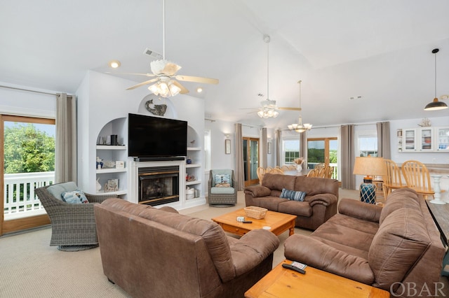 living room with built in shelves, ceiling fan with notable chandelier, a fireplace, visible vents, and vaulted ceiling