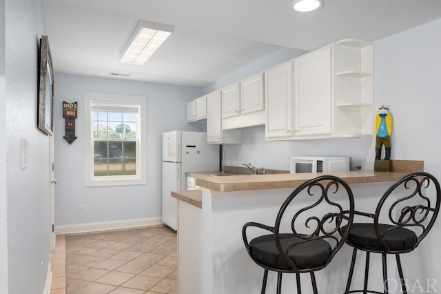 kitchen with a peninsula, a breakfast bar area, open shelves, and white cabinets