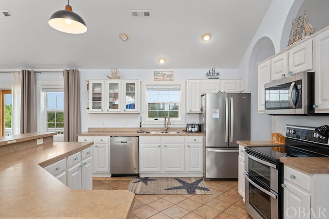 kitchen with decorative light fixtures, a sink, white cabinetry, appliances with stainless steel finishes, and glass insert cabinets