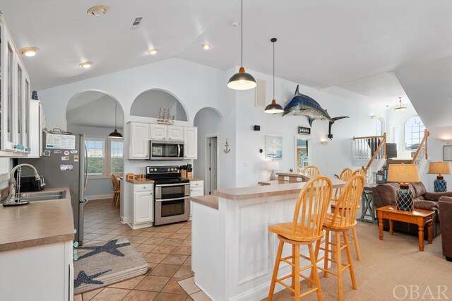 kitchen featuring glass insert cabinets, a sink, white cabinets, appliances with stainless steel finishes, and decorative light fixtures