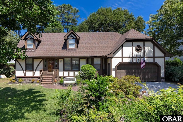718 Canal Dr Lot 308, Kill Devil Hills, NC 27948 - tudor house featuring a porch, an attached garage, a front yard, driveway, and roof with shingles