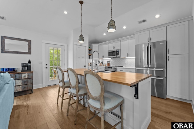 kitchen with appliances with stainless steel finishes, butcher block counters, a center island with sink, decorative backsplash, and a kitchen breakfast bar