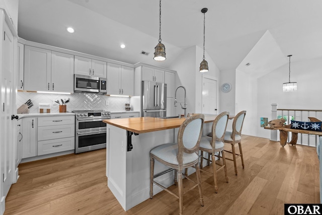kitchen with stainless steel appliances, wooden counters, a sink, tasteful backsplash, and a center island with sink