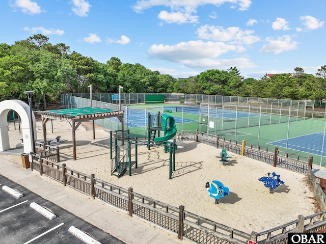view of property's community featuring fence, uncovered parking, a tennis court, and view of wooded area
