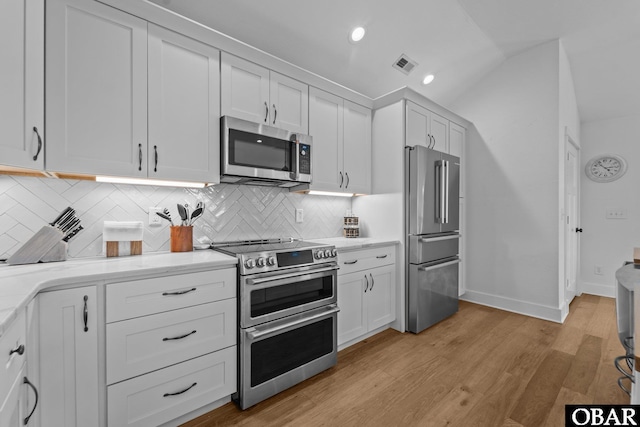 kitchen with stainless steel appliances, decorative backsplash, baseboards, white cabinetry, and lofted ceiling
