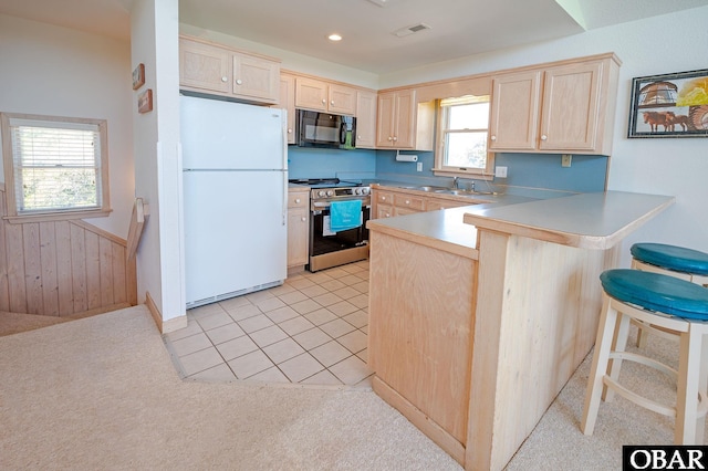 kitchen with freestanding refrigerator, black microwave, light brown cabinets, and stainless steel electric range oven