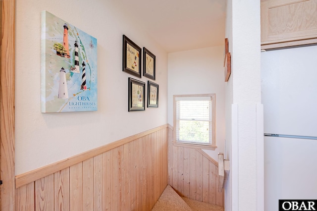 hallway with wainscoting, wooden walls, and an upstairs landing