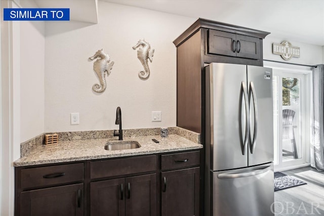 kitchen featuring freestanding refrigerator, a sink, dark brown cabinetry, and light stone countertops