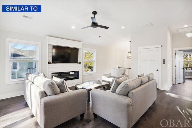 living room featuring baseboards, visible vents, a ceiling fan, a glass covered fireplace, and dark wood-type flooring