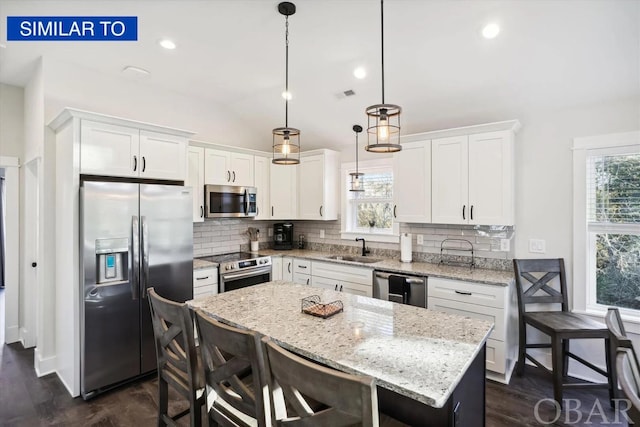 kitchen with stainless steel appliances, a breakfast bar, white cabinetry, hanging light fixtures, and a center island