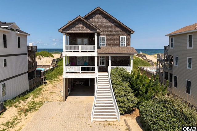 raised beach house featuring driveway, a carport, a water view, and a balcony