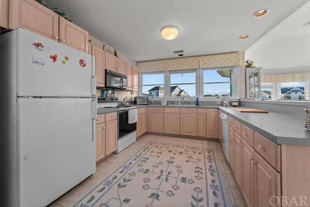 kitchen with light tile patterned floors, white appliances, a sink, light brown cabinetry, and dark countertops