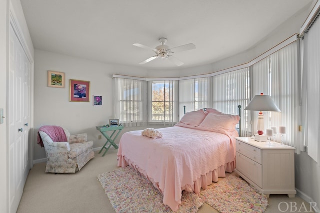 bedroom featuring baseboards, ceiling fan, a closet, and light colored carpet