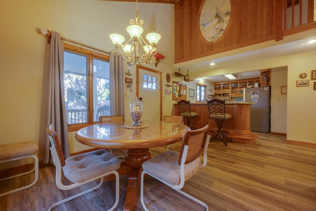 dining room featuring baseboards, a towering ceiling, light wood-style flooring, and an inviting chandelier