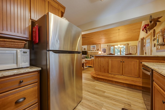 kitchen with brown cabinets, appliances with stainless steel finishes, light wood-style floors, and pendant lighting