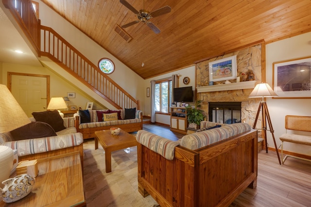 living area featuring a stone fireplace, wooden ceiling, light wood-style flooring, baseboards, and stairs