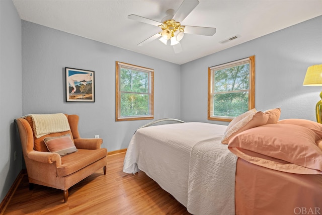 bedroom with baseboards, multiple windows, ceiling fan, and light wood finished floors