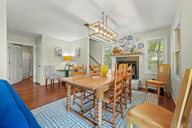 dining room with a wealth of natural light, stairs, wood finished floors, and a tile fireplace