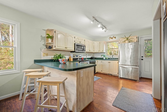 kitchen with stainless steel appliances, dark countertops, a sink, wood finished floors, and a peninsula