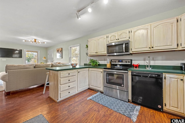 kitchen featuring dark countertops, open floor plan, dark wood-style flooring, a peninsula, and stainless steel appliances