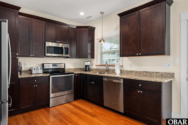 655 Pampas Ct Lot 162, Corolla, NC 27927 - kitchen featuring appliances with stainless steel finishes, light wood finished floors, light stone counters, decorative light fixtures, and dark brown cabinetry
