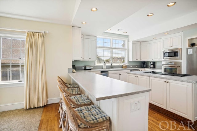 kitchen featuring a kitchen breakfast bar, stainless steel appliances, light countertops, and white cabinets