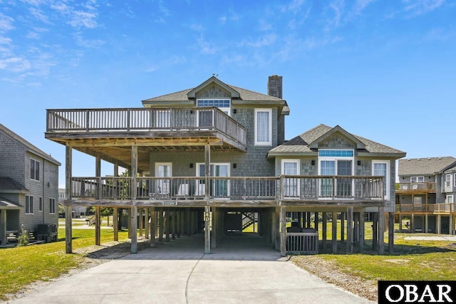 raised beach house featuring roof with shingles, a chimney, a carport, driveway, and a wooden deck