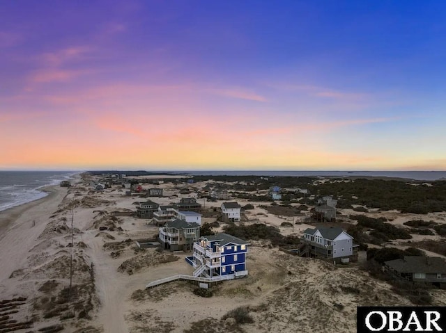 aerial view at dusk with a water view and a beach view