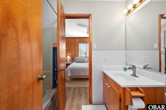 full bath featuring connected bathroom, vanity, wainscoting, wood finished floors, and tile walls