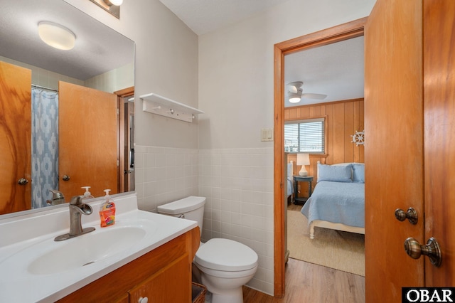 ensuite bathroom featuring a wainscoted wall, toilet, wood finished floors, tile walls, and vanity