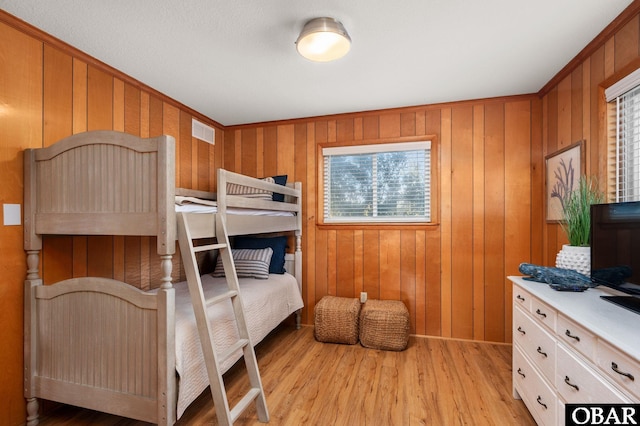 bedroom featuring light wood finished floors, visible vents, and wooden walls