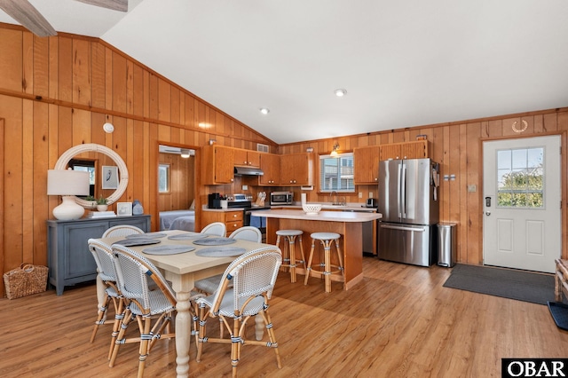 dining room with vaulted ceiling, light wood-style floors, and wood walls