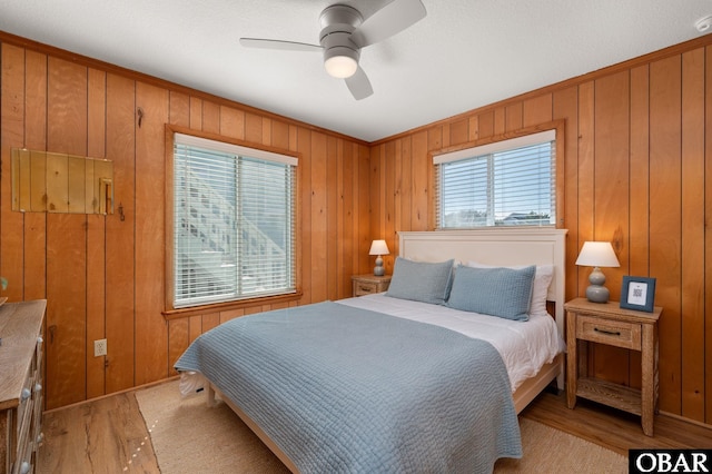 bedroom featuring light wood finished floors, wooden walls, and ceiling fan