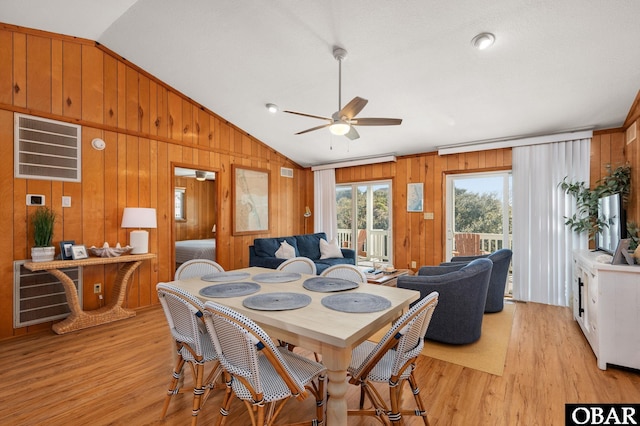 dining space featuring wooden walls, visible vents, light wood finished floors, ceiling fan, and vaulted ceiling