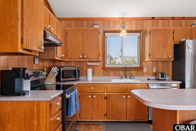 kitchen with under cabinet range hood, light countertops, brown cabinets, appliances with stainless steel finishes, and a sink