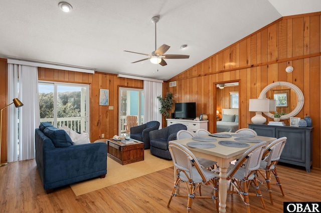 dining space with visible vents, a ceiling fan, light wood-style floors, wood walls, and vaulted ceiling