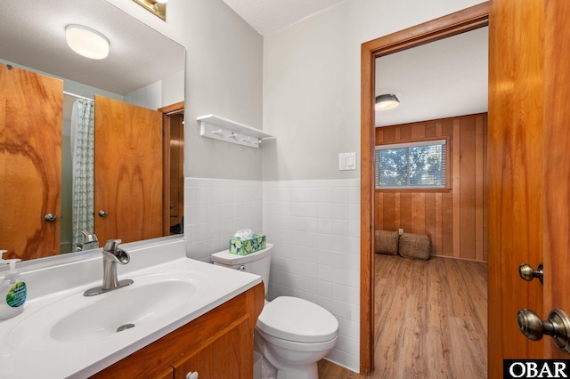 full bathroom featuring a wainscoted wall, toilet, wood finished floors, tile walls, and vanity