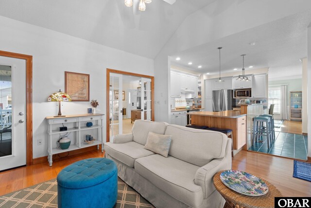 living room with baseboards, a ceiling fan, light wood-style flooring, vaulted ceiling, and recessed lighting