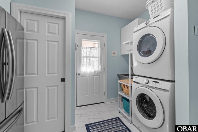 laundry area featuring stacked washer / dryer, laundry area, marble finish floor, and baseboards