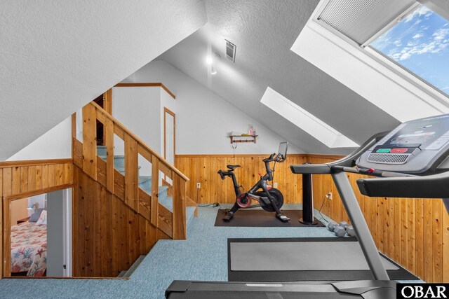 workout room with carpet floors, vaulted ceiling with skylight, wainscoting, and wood walls