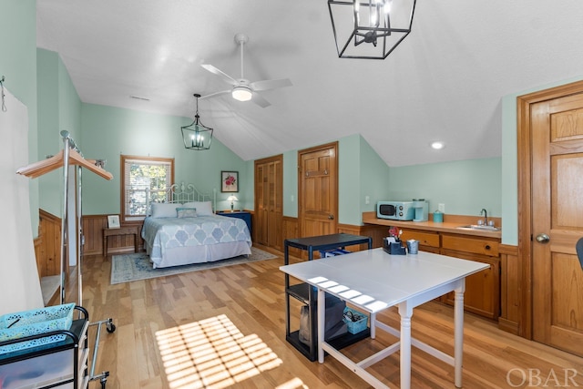 bedroom with a wainscoted wall, light wood finished floors, vaulted ceiling, and a sink