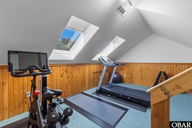 workout room featuring wood walls, lofted ceiling with skylight, carpet, and visible vents